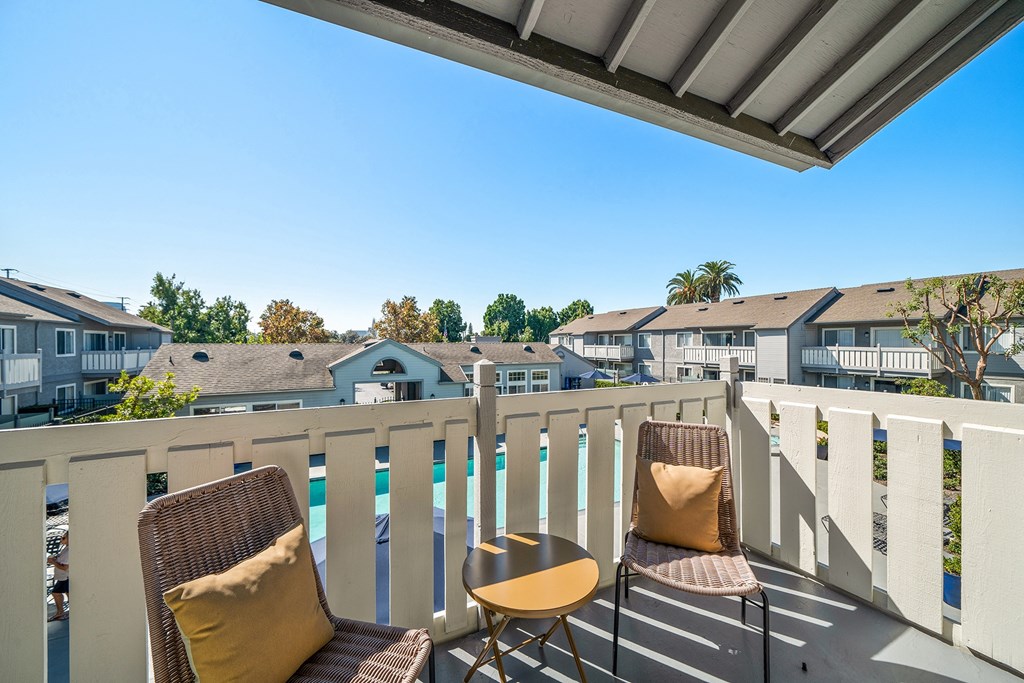 two chairs on a balcony overlooking a pool and houses