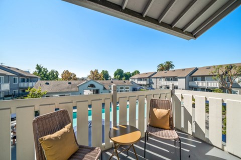 two chairs on a balcony overlooking a pool and houses