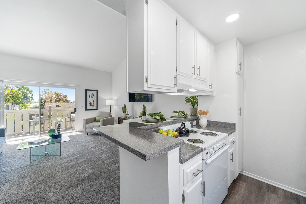 an open kitchen and living room with white cabinets and granite counter tops