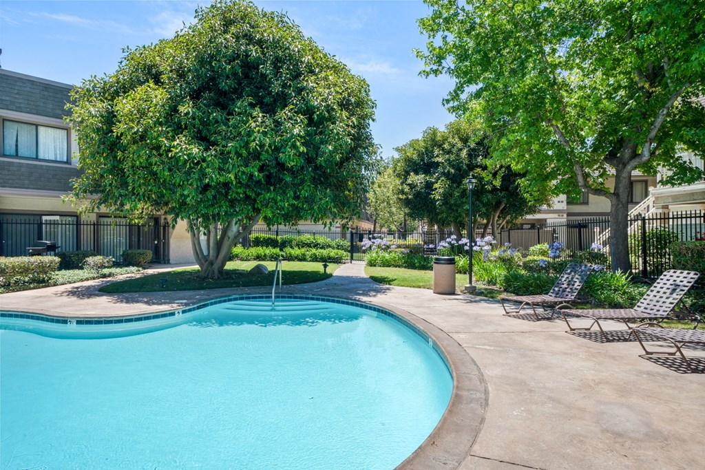 a swimming pool with chairs and trees in front of a building