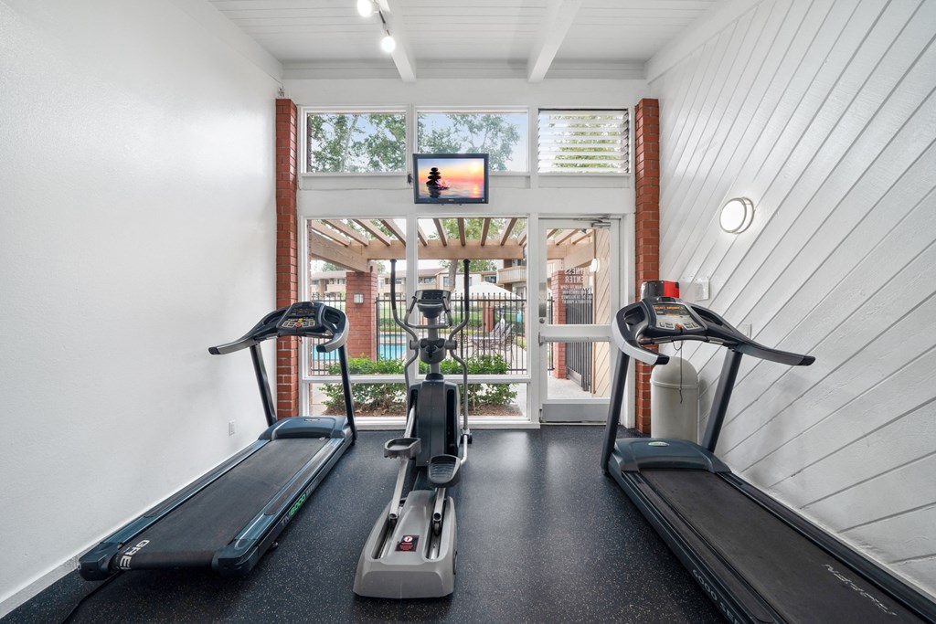 two treadmills and yoga machines in a gym with a view of a window
