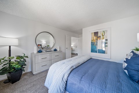 A bedroom with a blue bedspread and a mirror on the wall.