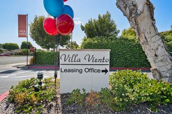 a sign for the villa victoria leasing office next to a tree with balloons