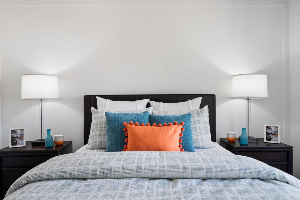 a bedroom with a bed with blue and orange pillows and two lamps
