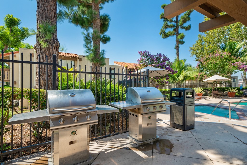 two bbq grills next to a swimming pool with trees