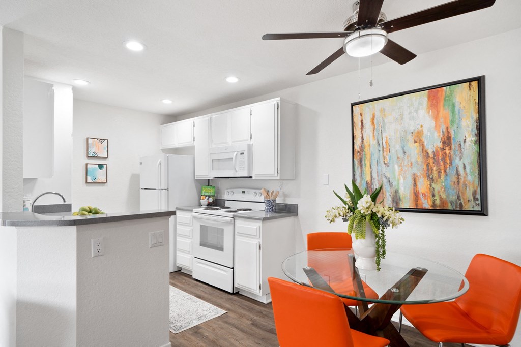 a white kitchen and dining room with orange chairs and a table