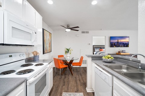 a kitchen with white appliances and a dining room with orange chairs