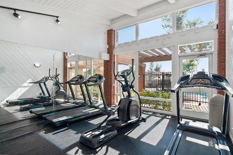 two treadmills and other exercise equipment in a gym with glass doors and windows