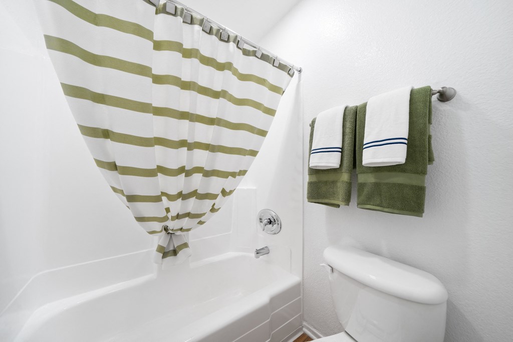 a bathroom with a white toilet and a green and white striped shower curtain