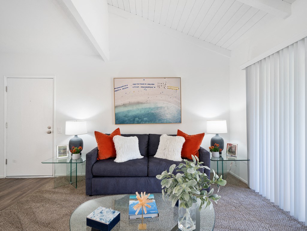 a living room with white walls and a dark blue couch with orange and white pillows