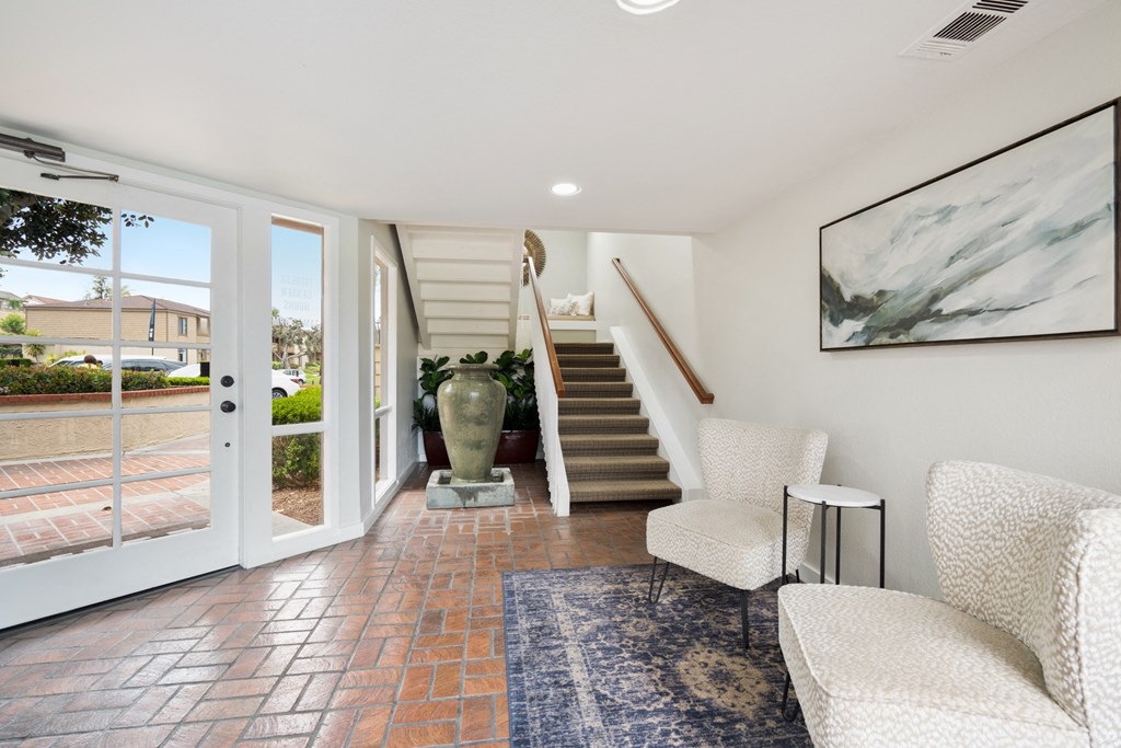 a living room with white chairs and a staircase and a glass door