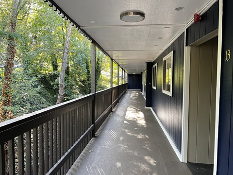 A long balcony with a railing and a view of trees.