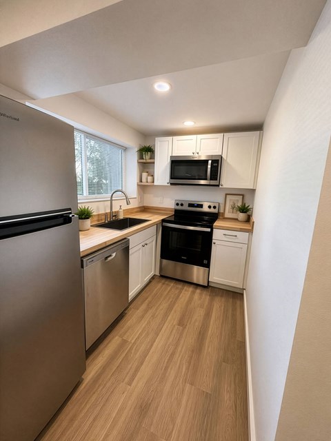 A modern kitchen with stainless steel appliances and wooden flooring.