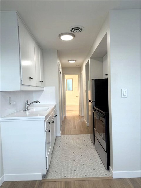 A kitchen with white cabinets and a black refrigerator.