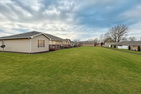 A large grassy field with a few houses in the background.