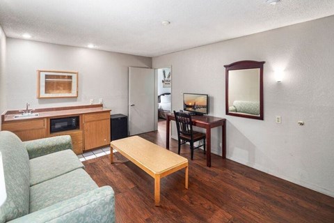 A living room with a couch, a coffee table, a dining table, and a kitchen area in the background.
