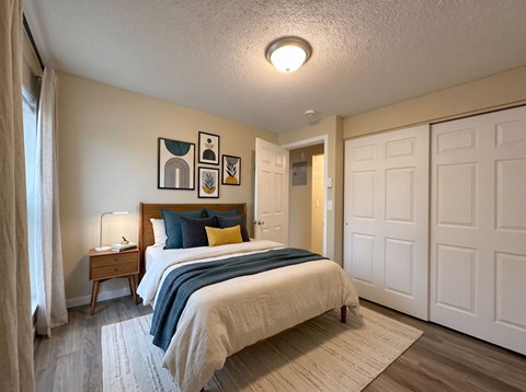 A bedroom with a bed, nightstand, and artwork on the wall.