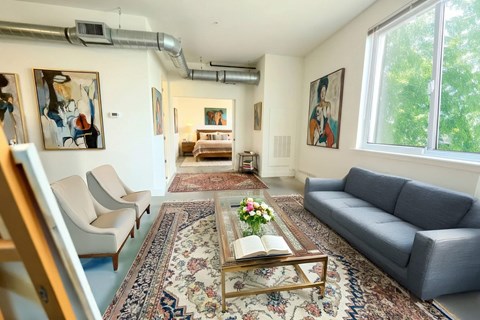 A living room with a grey couch, a coffee table with a book and flowers on it, and a painting on the wall.
