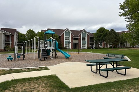 A playground with a green slide and picnic table in front of apartment buildings.