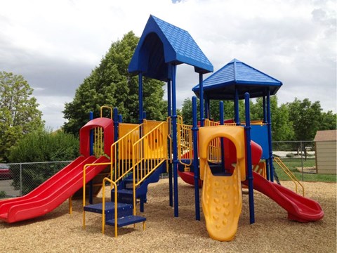A playground with a red slide, yellow stairs, and blue towers.