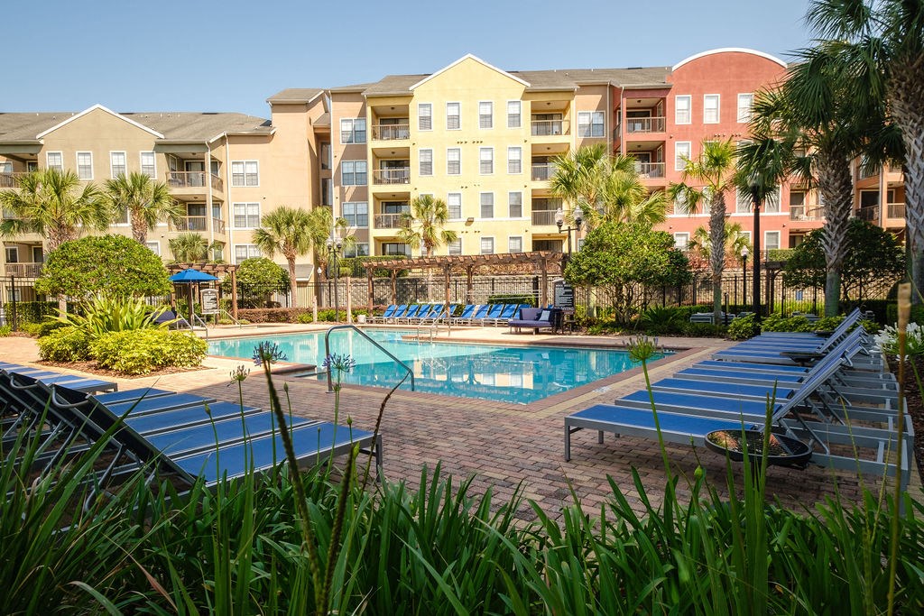 a swimming pool with blue lounge chairs in front of an apartment building