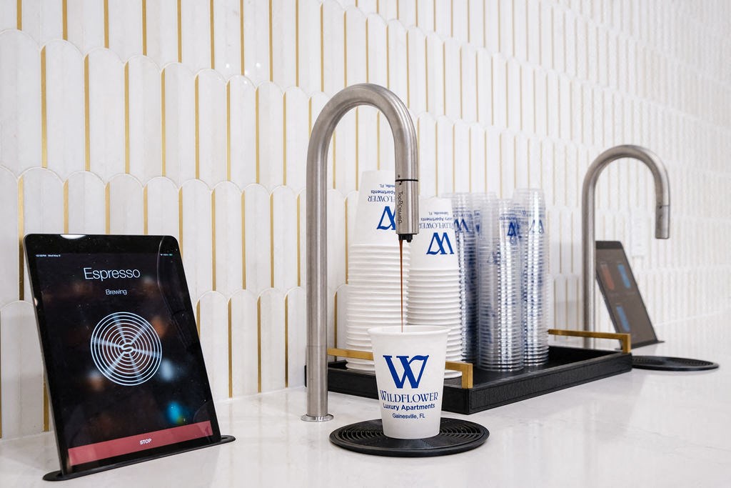 a cup of coffee sitting under a water faucet next to a tablet