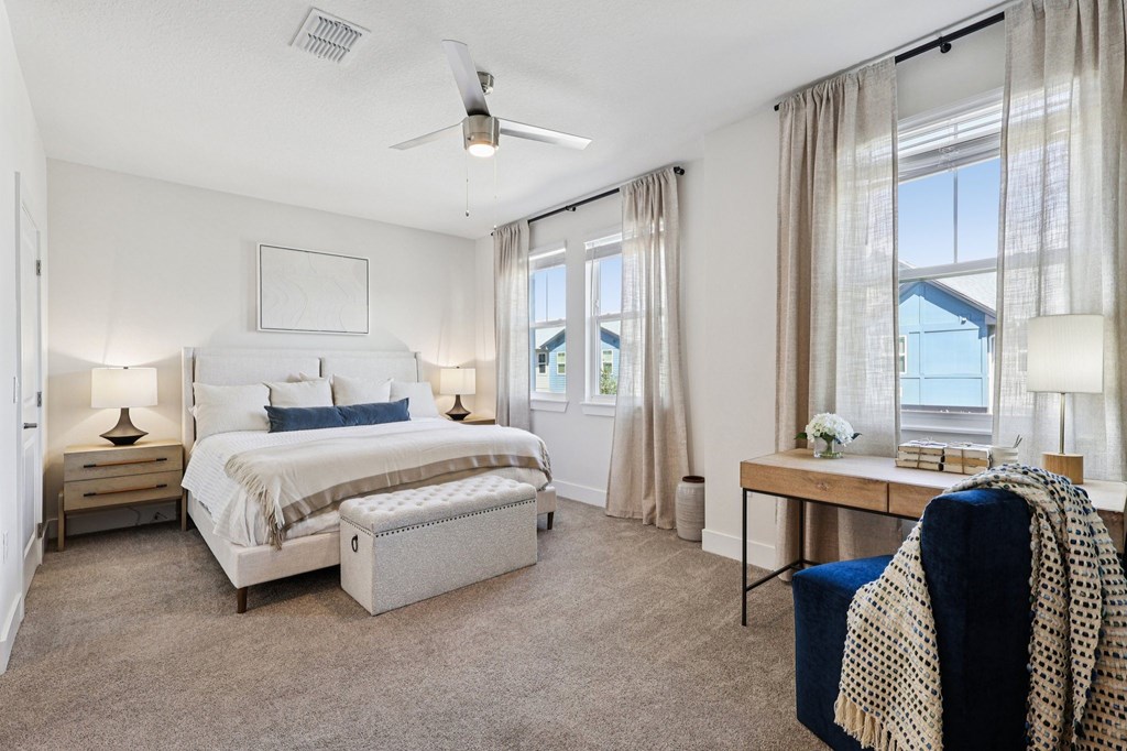 A bedroom with a large bed, a chair, and a table with a vase of flowers on it.