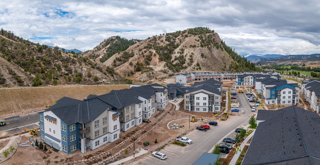A construction site with a large building under construction in the foreground and a mountain in the background.