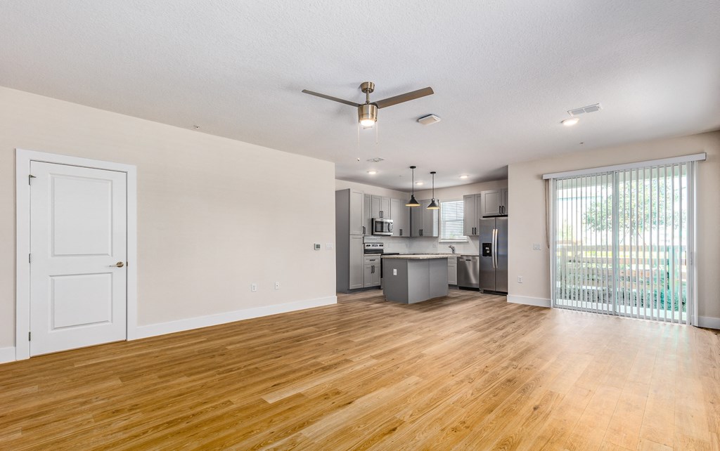 the living room and kitchen of an apartment with wood flooring and a ceiling fan