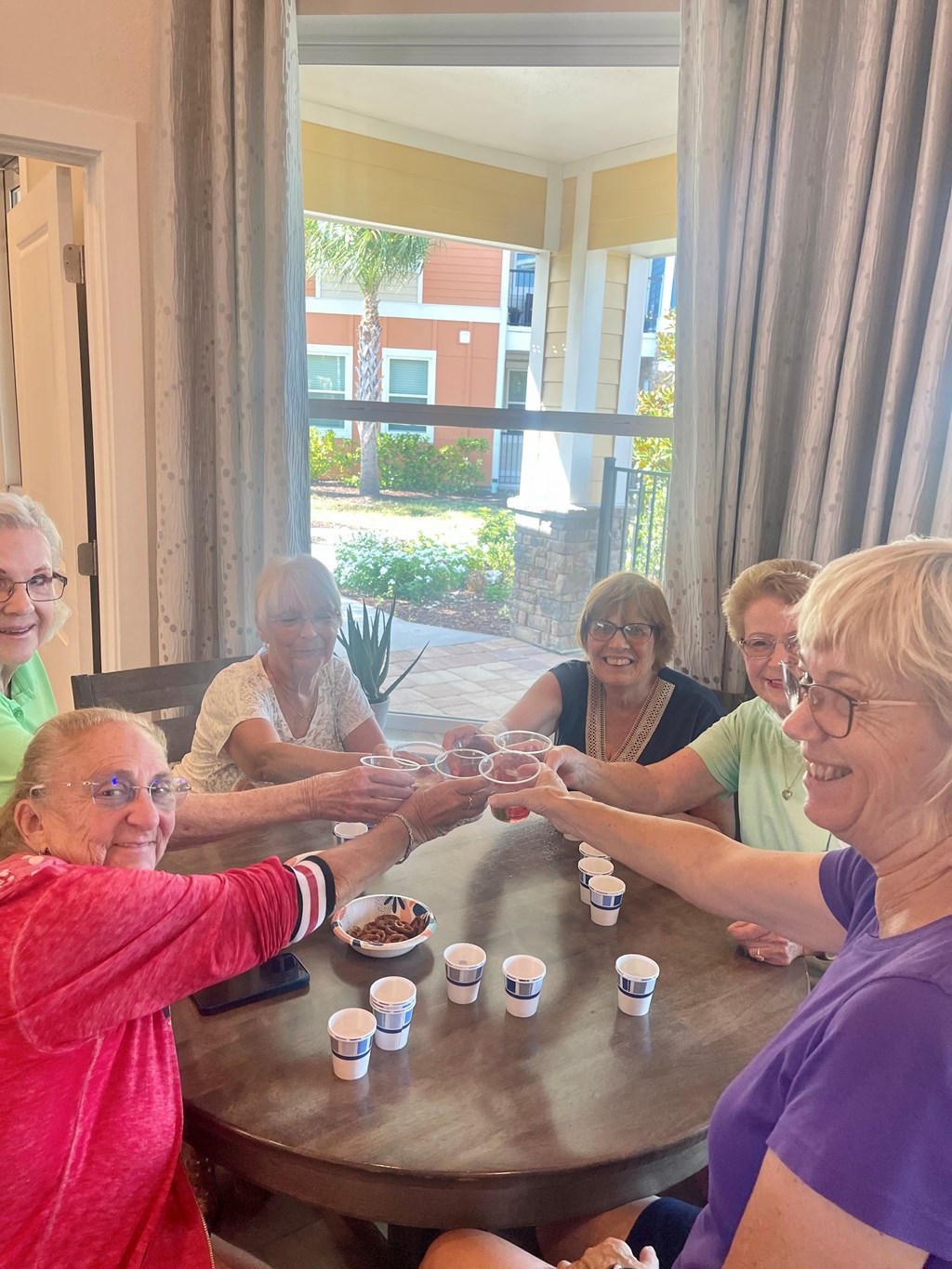 A group of elderly women are playing a game with small cups.