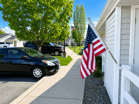 A black car is parked on a driveway next to a house with an American flag hanging from the porch.