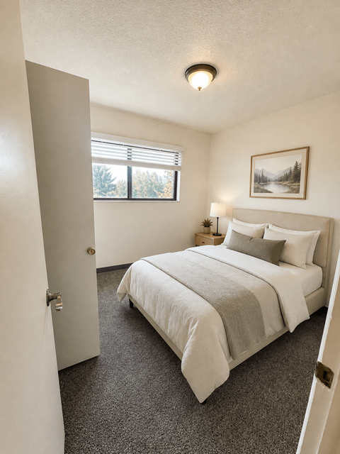 A bedroom with a bed, pillows, a nightstand, and a window.