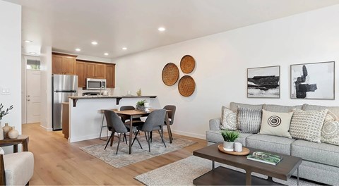 A modern living room with a grey couch, a dining table with chairs, and a kitchen area in the background.