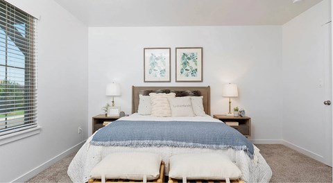 A bedroom with a bed, two lamps, and two framed pictures on the wall.