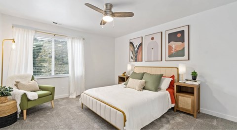 A bedroom with a bed, a green chair, and a ceiling fan.