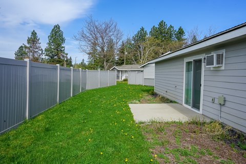 A grey fence separates a green lawn from a grey house.