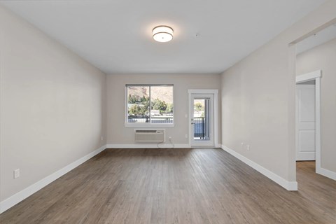 A spacious room with light wood flooring and a window overlooking a balcony.