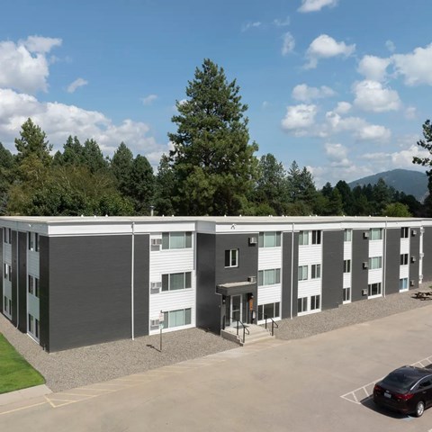 A car is parked in the parking lot of a modern building with a mountain in the background.