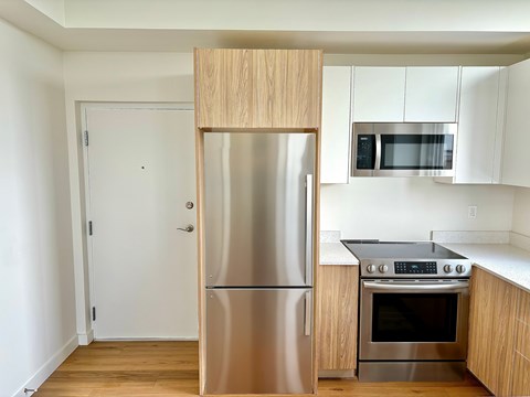 A kitchen with a stainless steel refrigerator and oven, wooden cabinets, and a white door.