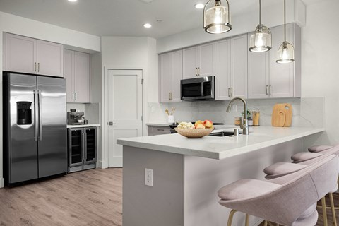 A kitchen with a refrigerator, microwave, and a counter with a bowl of fruit on it.