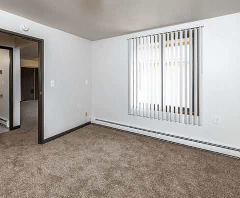A room with a carpeted floor and a window with blinds.