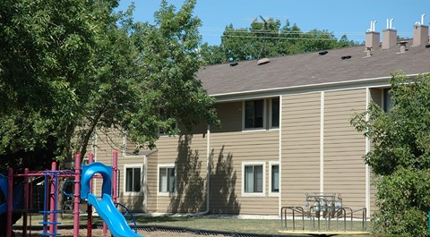 A playground with a blue slide in front of a beige house.