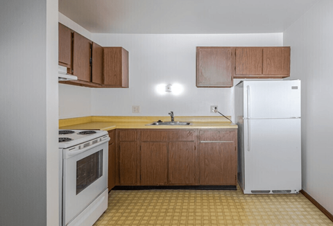 A kitchen with a white refrigerator, white stove, and brown cabinets.