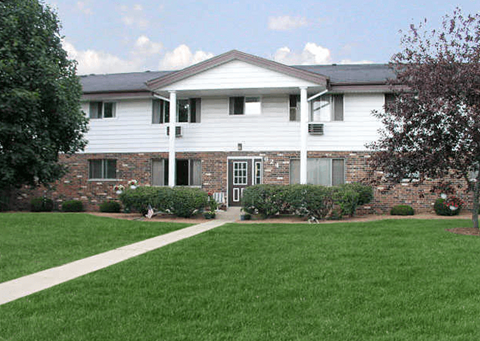 A white house with a brick wall and a green lawn in front.