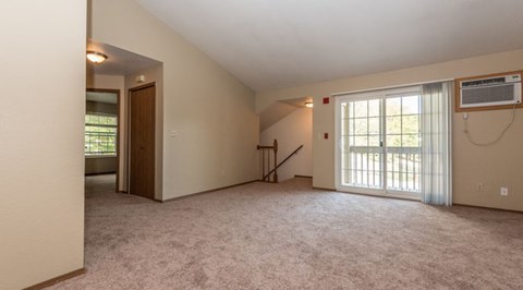 A spacious room with carpeted floor, a staircase, and a window with blinds.