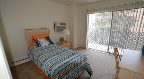 A bedroom with a bed, desk, and window with blinds.