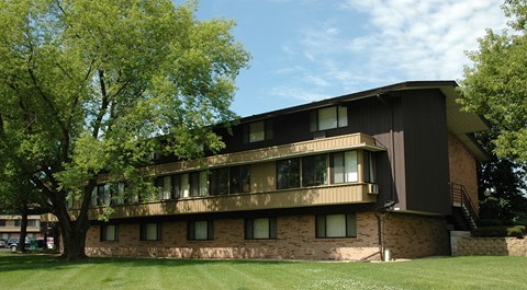 A large brown building with a balcony on the second floor is surrounded by trees.