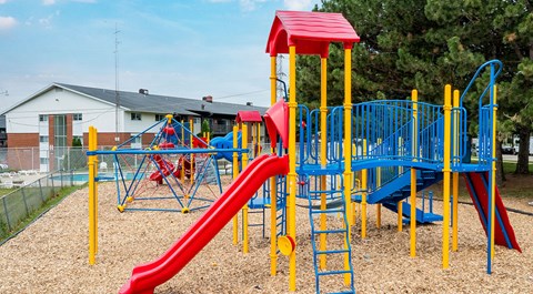 A playground with a red and blue slide and yellow safety bars.