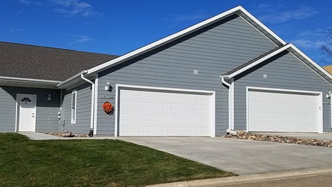 A grey house with two garages and a red flower on the door.