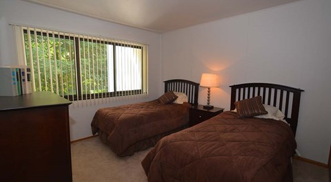 Two twin beds in a room with a window and a nightstand with a lamp.